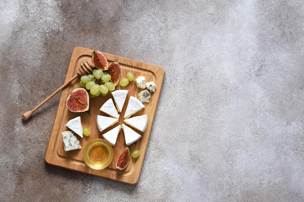 Foto piatto di formaggio camembert e formaggio blu con uva, fichi, miele su una tavola di legno. piatto di formaggi