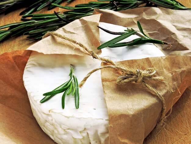 Camembert cheese in paper and fresh rosemary.