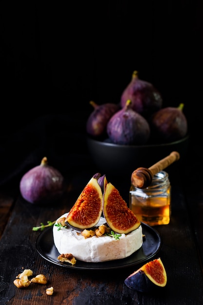 Camembert cheese with figs, walnuts, honey and thyme served for a dinner in dark key.