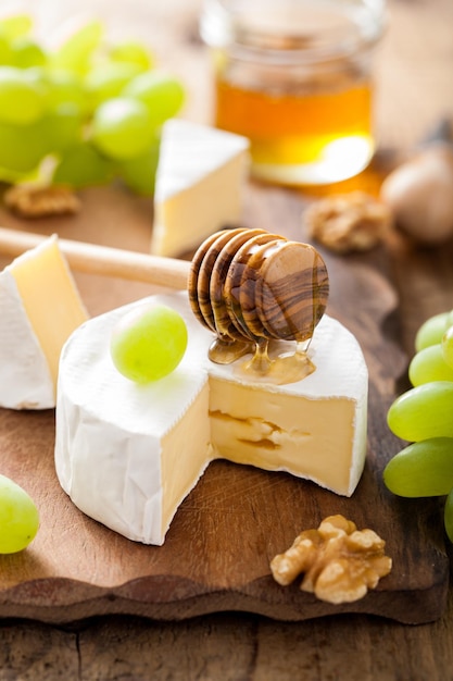 camembert cheese with grapes honey and nuts on wooden background