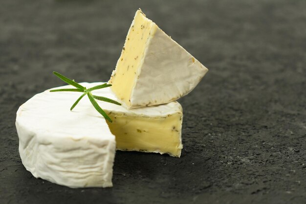 Camembert cheese with herbs garnished with a sprig of rosemary on a black background