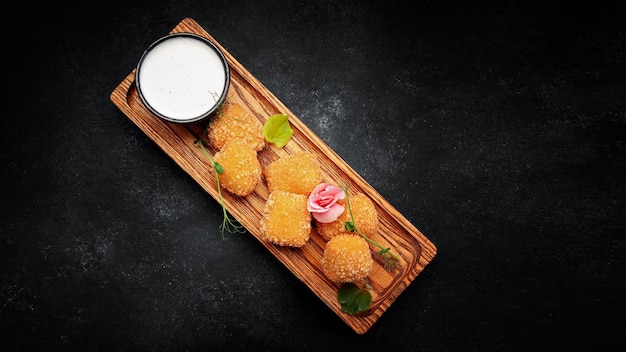 Camembert fries with sauce on a wooden board on a dark background