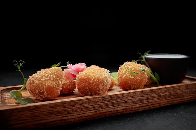 Camembert fries with sauce on a wooden board on a dark background