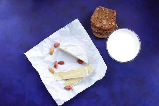 Camembert met noten donker brood en een glas melk op een blauwe achtergrond Een geweldig product voor een ontbijt Heerlijke kaas op perkamentpapier close-up