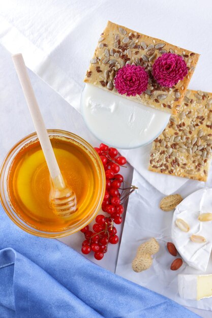 Foto bacche di camembert e biscotti con semi su carta pergamena bianca formaggio con miele un bicchiere di latte e un tovagliolo blu e bianco su sfondo chiaro primo piano