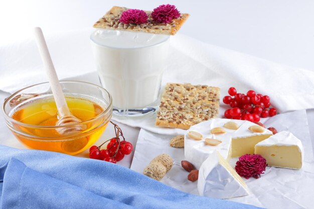Camembert nuts berries and biscuits with seeds on white parchment paper Cheese with honey a glass of milk and a blue and white napkin on a light background Closeup