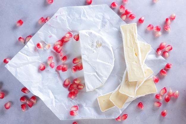 Camembert and pomegranate seeds on parchment paper on a light background Delicious cheese on the table closeup A great product for a breakfast