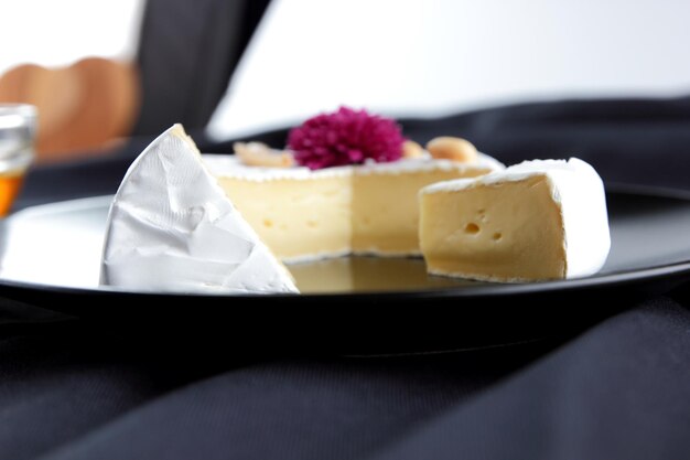 Camembert with nuts on a black plate Closeup of cheese with rose flower and honey on black background