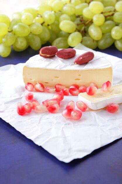 Camembert with pomegranate seeds green grapes and nuts on a blue background Delicious cheese on parchment paper close up