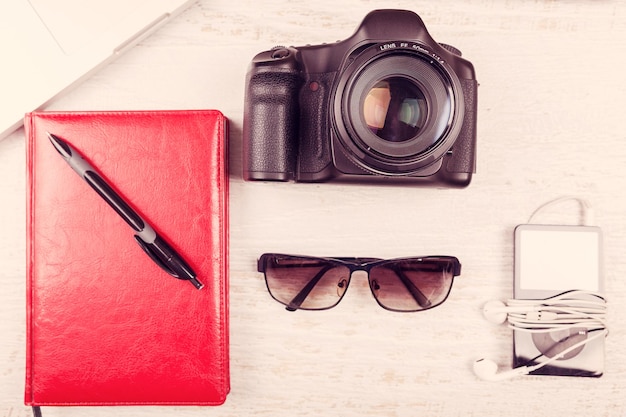 Camera, laptop, digital tabler, writing notebook and sunglasses on wooden background. Hipster vintage style