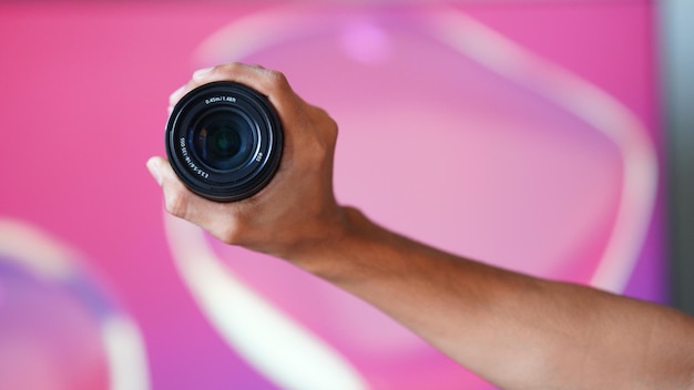 Camera lens holding in hand with pink background