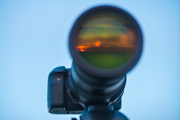 The camera lens with a sunset reflection on the background of the sky