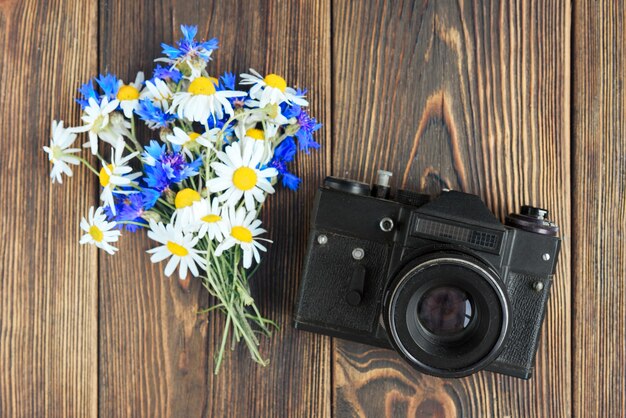 Фотоаппарат, ноутбук, мобильный телефон и полевые цветы на темном деревянном фоне. фриланс. заработок на фото.