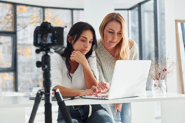 Camera op statief neemt op Twee jonge vrouwelijke freelancers die binnenshuis op kantoor werken met laptop