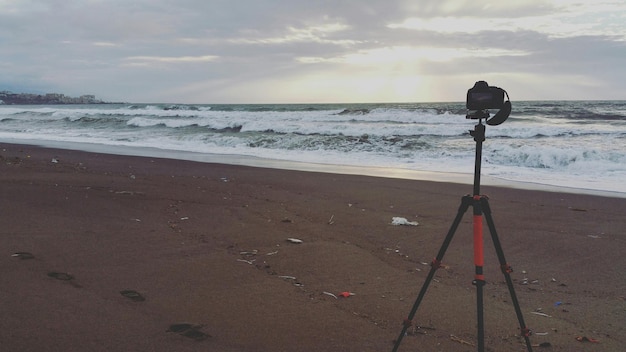 Foto fotocamera e treppiede sulla spiaggia durante il tramonto