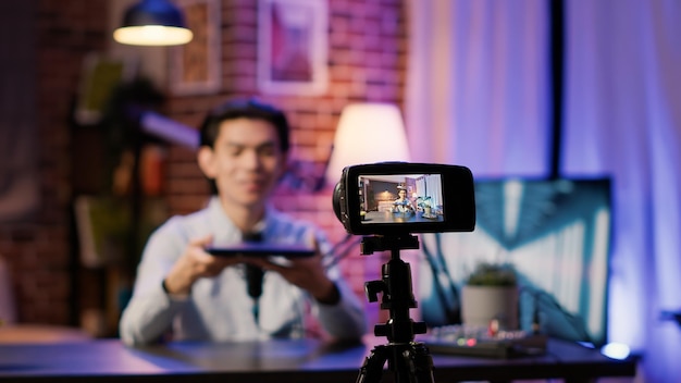 Camera on tripod filming podcast show with man doing product\
review of laptop, social media content. live broadcasting video\
with wireless computer recommendation on online channel.