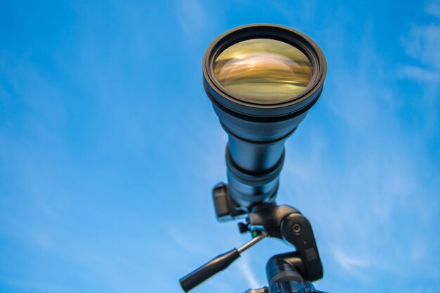 Photo the camera with a telephoto lens on the blue sky background