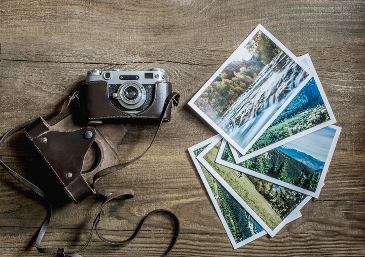 A camera on wooden boards. The old camera lies on a wooden background near pictures with a landscape. View from above