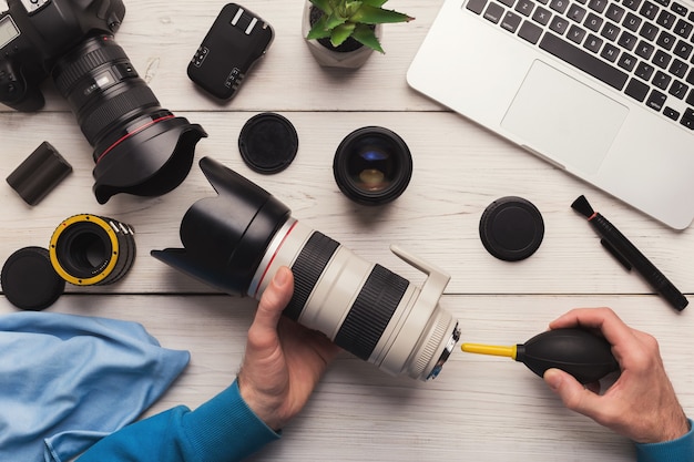 Cameralens schoonmaken met speciaal gereedschap, close-up. Fotograaf handen vegen lens op werkplek. Zorg voor professionele fotoapparatuur, technologieconcept