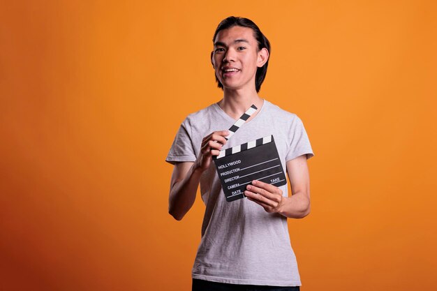 Cameraman assistant holding film making clapperboard, movie\
scene shooting. cinematography, filmmaking, video production, young\
smiling asian clapper loader slapping slate