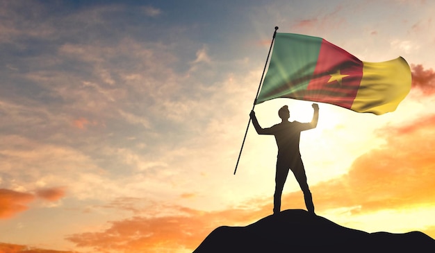 Cameroon flag being waved by a man celebrating success at the top of a mountain 3D Rendering