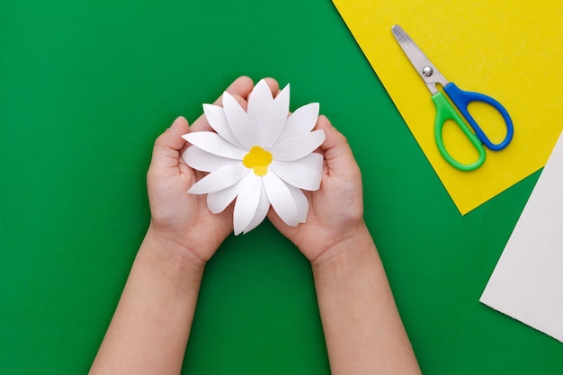 Photo camomile paper craft in child hands on green background