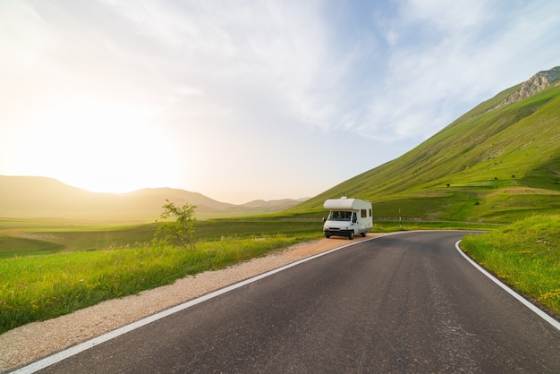 Camper aan de kant van de weg in prachtig landschap. Dramatische hemel bij zonsondergang, schilderachtige wolken boven unieke hooglanden en heuvelruggen in Italië, alternatief vanlife-vakantieconcept.