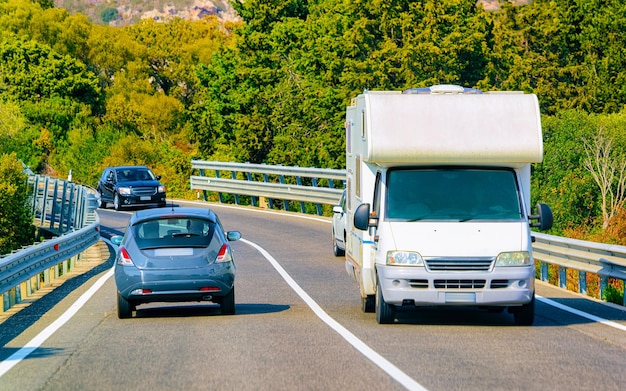 Camper en auto's op de weg aan de Costa Smeralda aan de Middellandse Zee in de zomer van het eiland Sardinië, Italië. Caravan camper op vakantie aan snelweg. Minivan rv op snelweg. Gemengde media.