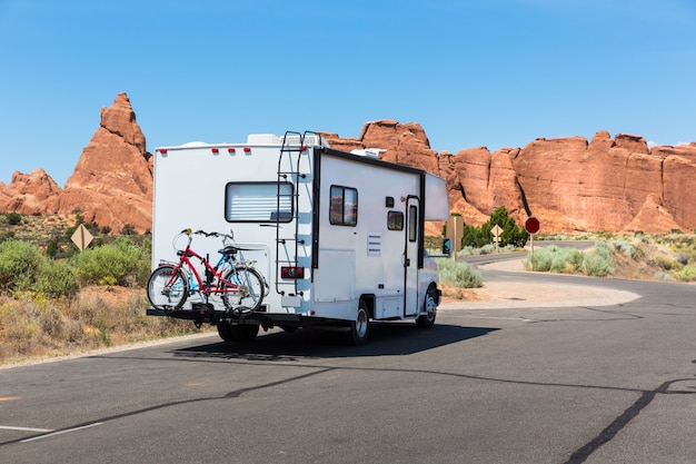 Camper with bikes on asphalt road. Rocky mountains on the background.