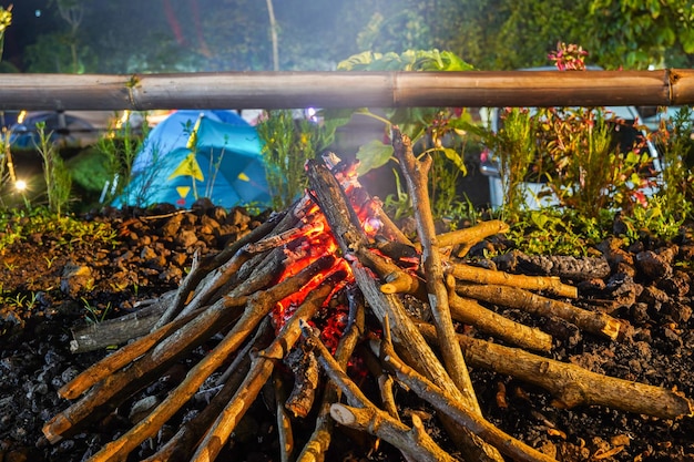 A campfire is lit up by a blue tent.