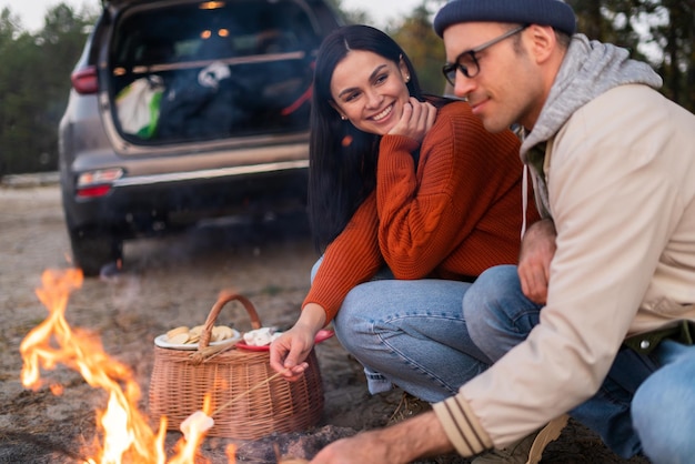 Campfire outdoor fun. Happy young friends at camp or picnic, enjoying roasting marshmallow at fire, sitting near the bonfires in a wood, warming and talking