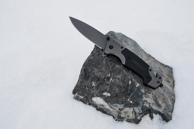 Складной нож для кемпинга зимой лежит на камнеАктивный отдых в походах и путешествиях