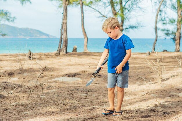 Camping people outdoor lifestyle tourists summer forest near lazur sea Blond boy play study survival techniques practice methods to dig the earth with a shovel Natural children education