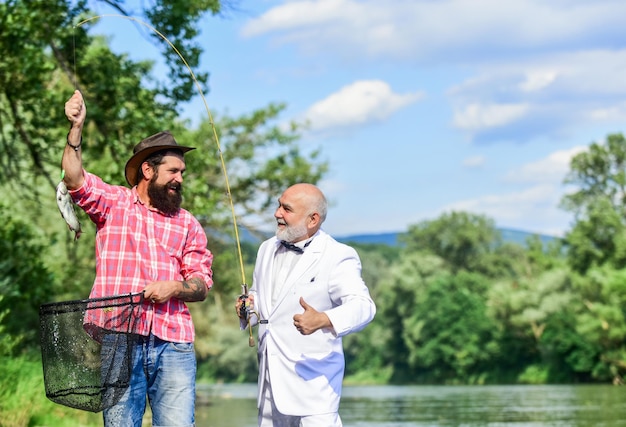 Camping on the shore fly fish hobby of businessman retirement fishery retired dad and mature bearded son happy fishermen friendship Catching and fishing concept Two friends fishing together