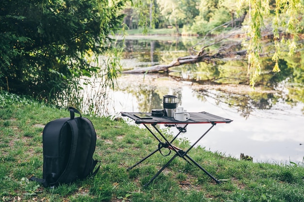 Camping table with cup of coffee and rucksack outdoors