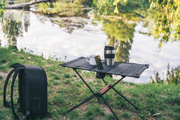 Photo camping table with cup of coffee and smartphone outdoors everyday technology picturesque landscape recreation and travel concept