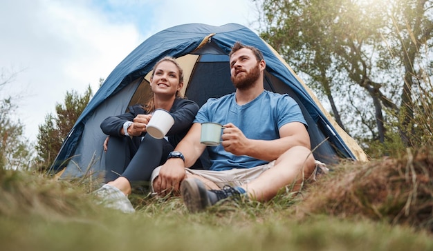 Camping tent and nature couple with coffee tea or hot chocolate relax in outdoor forest or woods Grass field trees morning view and camper people bond talk or enjoy quality time peace or freedom