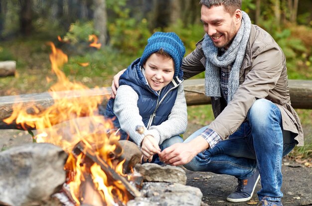 Camping, tourism, hike, family and people concept - happy\
father and son roasting marshmallow over campfire