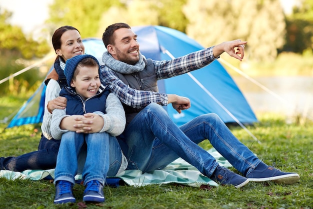 camping, tourism, hike and people concept - happy family over tent at camp site pointing finger to something