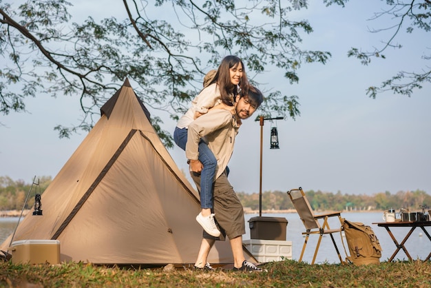 キャンプと旅行のコンセプト若いカップルはガールフレンドをピギーバックで運び、湖を見ながら歩く