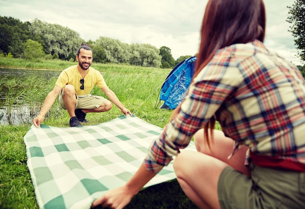 Foto concetto di campeggio, viaggi, turismo, escursione e persone - coppia felice che posa coperta da picnic al campeggio