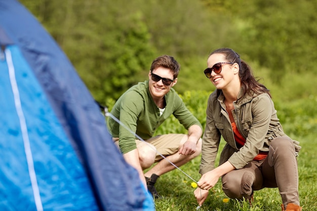 camping, travel, tourism, hike and people concept - happy couple setting up tent outdoors