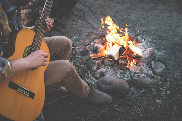 Camping in the woods man plays the guitar by the fire in nature summer camping relaxation in nature