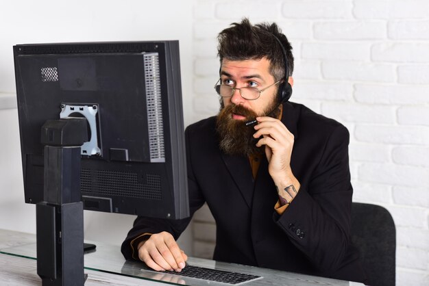 Foto posso aiutarti rispondere alle chiamate dei clienti operatore di call center al lavoro uomo barbuto che lavora in ufficio uomo con barba lunga e cuffie rappresentante barbuto dell'azienda al computer