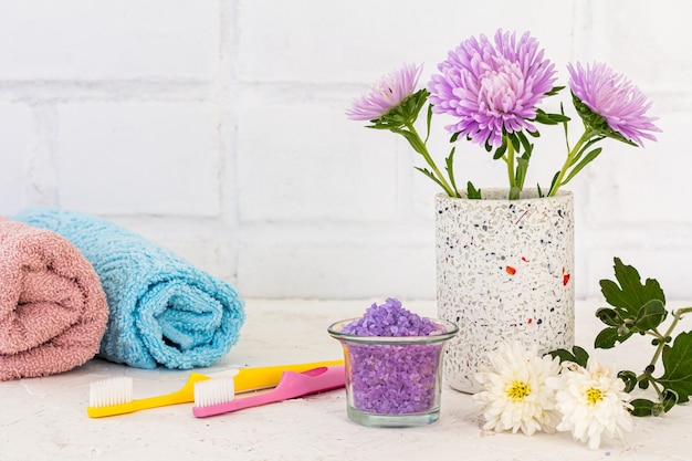 can with flowers of asters, towels, sea salt and toothbrushes on white background