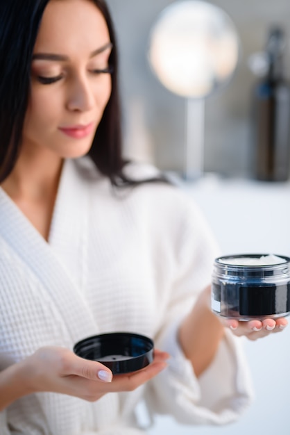 A  can with hair care in hand with a chic lady in a white gown, in the bathroom