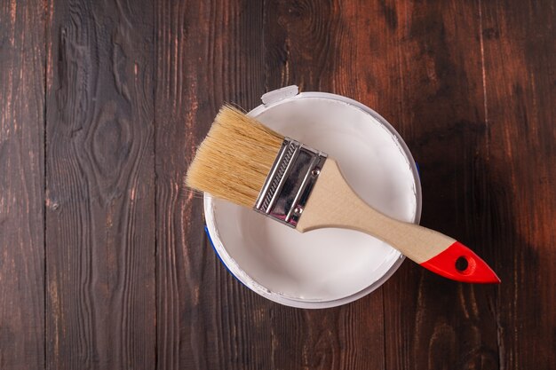 Can with paint of white color and paintbrush on brown wooden table