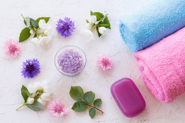 Can with sea salt, towels, soap and flowers of jasmine and cornflowers on a white surface