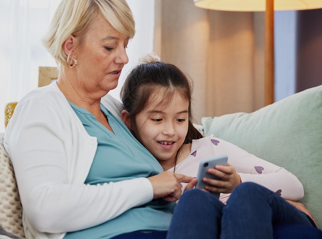 Can you download this game for me gran Shot of a little girl using a cellphone while sitting at home with her grandmother