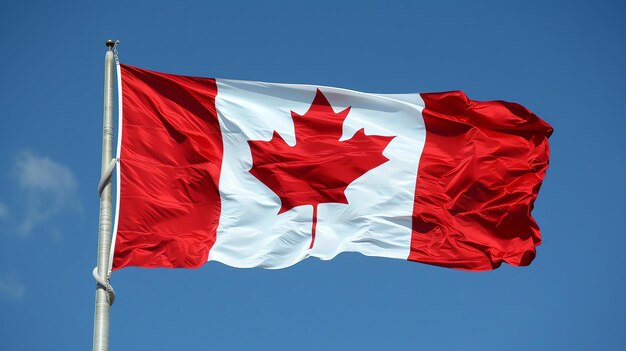 A Canadian flag is waving in the wind against a clear blue sky The flag is red and white with a red maple leaf in the center